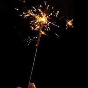 A sparkling hand-held sparkler illuminating against a black night sky, creating festive sparks.